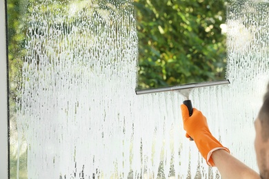 Photo of Male janitor cleaning window with squeegee, closeup