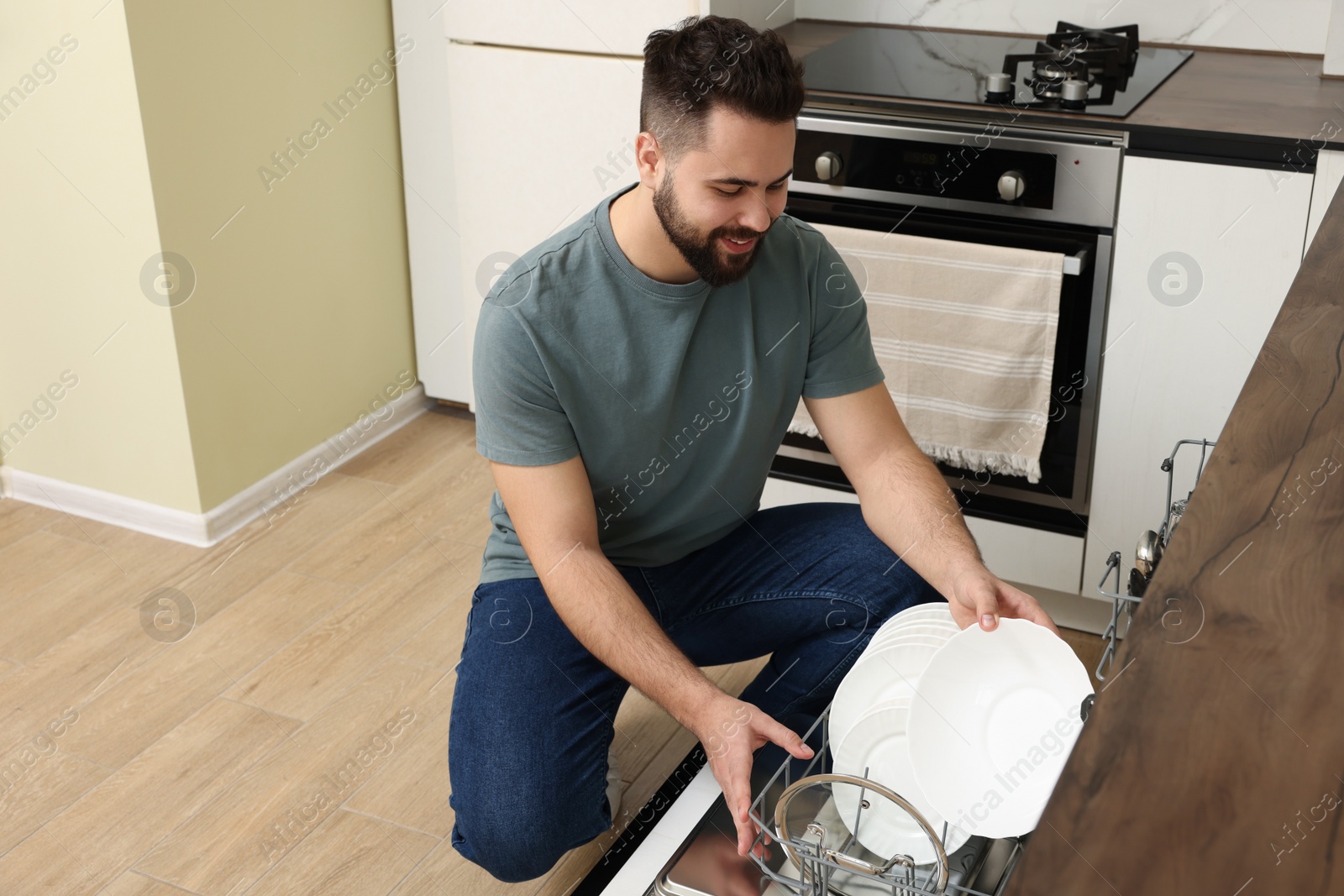 Photo of Smiling man loading dishwasher with plates in kitchen. Space for text