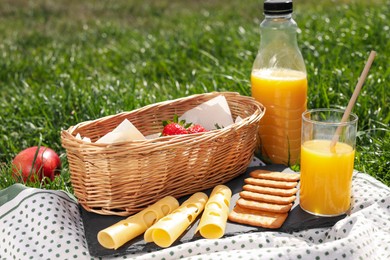 Blanket with juice and snacks for picnic on green grass