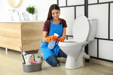 Young woman cleaning toilet bowl in bathroom