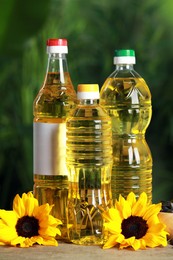 Photo of Bottles of cooking oil, sunflowers and seeds on wooden table against blurred background