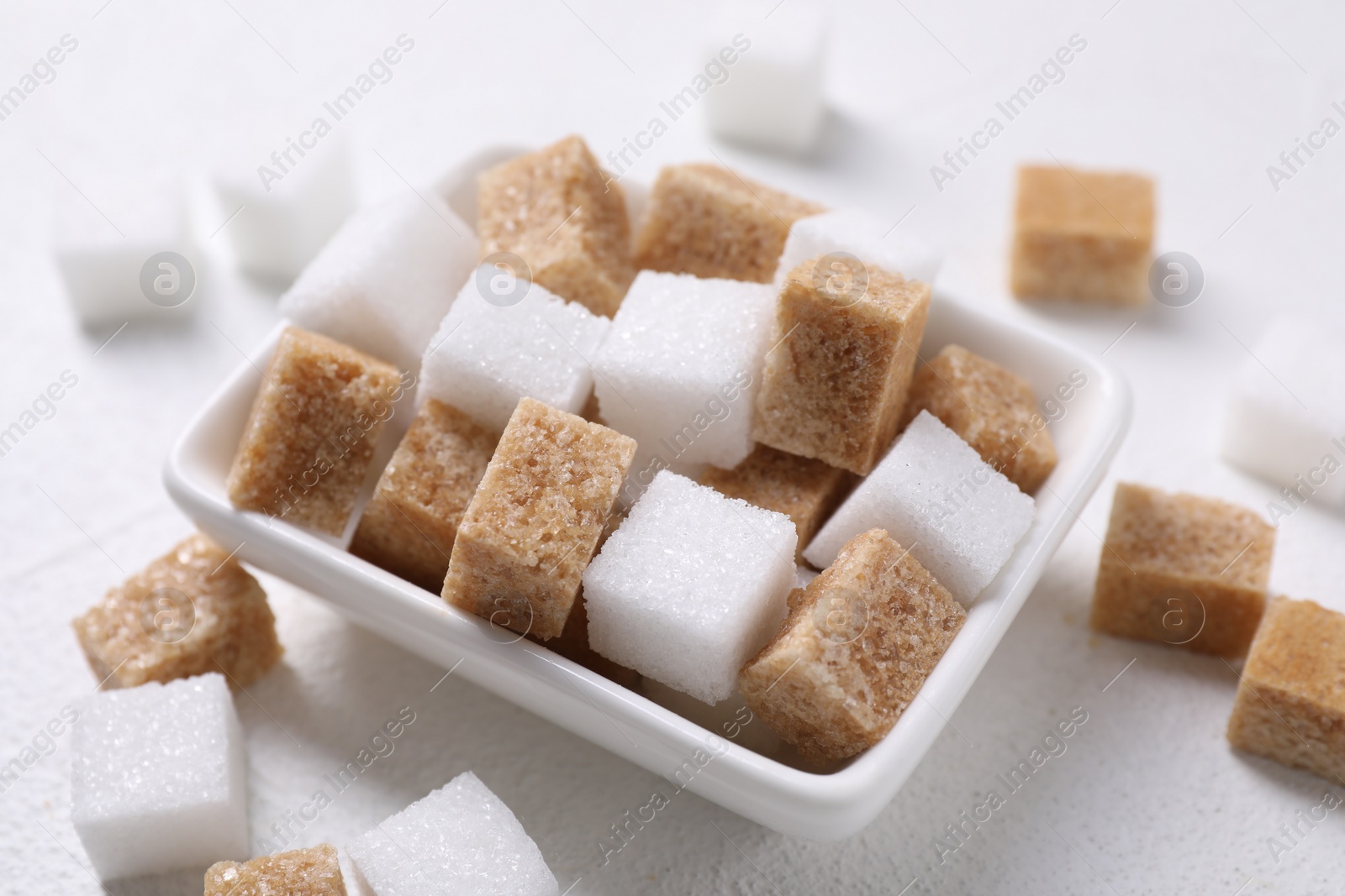 Photo of Different sugar cubes in bowl on white table, closeup