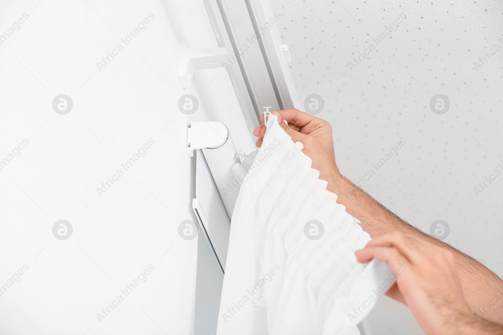 Photo of Young man hanging window curtain in room, closeup