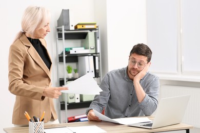 Photo of Serious boss and confused employee with documents at wooden table in office