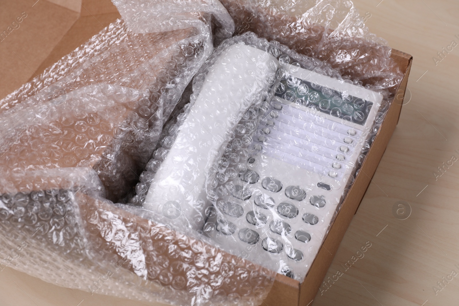 Photo of Corded phone with bubble wrap in cardboard box on wooden table, closeup