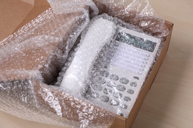 Corded phone with bubble wrap in cardboard box on wooden table, closeup