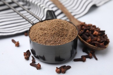 Photo of Aromatic clove powder in scoop and dried buds on white table, closeup