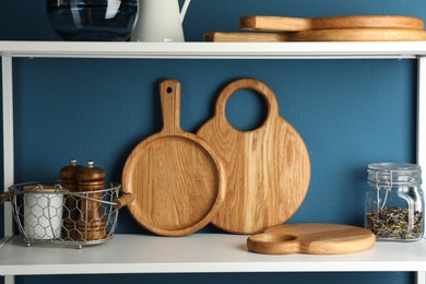 Wooden cutting boards, kitchen utensils and dry tea on shelving unit near blue wall