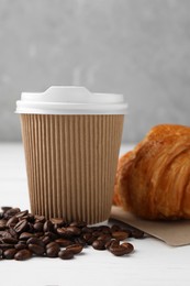 Photo of Coffee to go. Paper cup with tasty drink, croissant and beans on white table