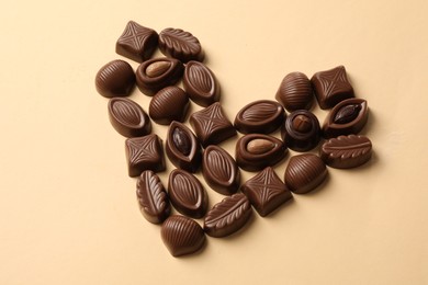 Photo of Heart made with delicious chocolate candies on beige background, above view