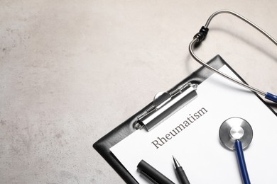 Photo of Clipboard with word Rheumatism and stethoscope on light gray textured table, space for text