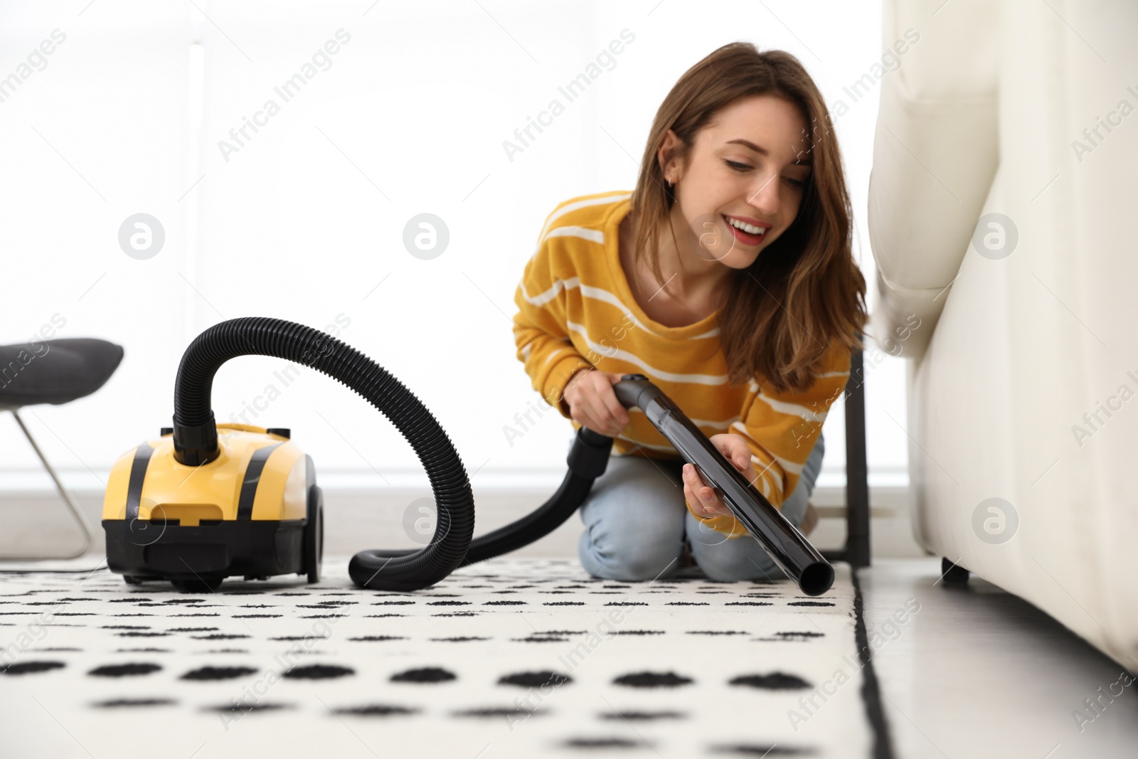 Photo of Young woman using vacuum cleaner at home