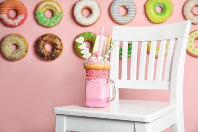 Photo of Tasty milk shake with sweets in mason jar on chair indoors