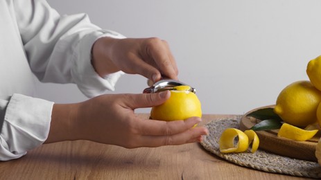 Woman zesting lemon at wooden table, closeup