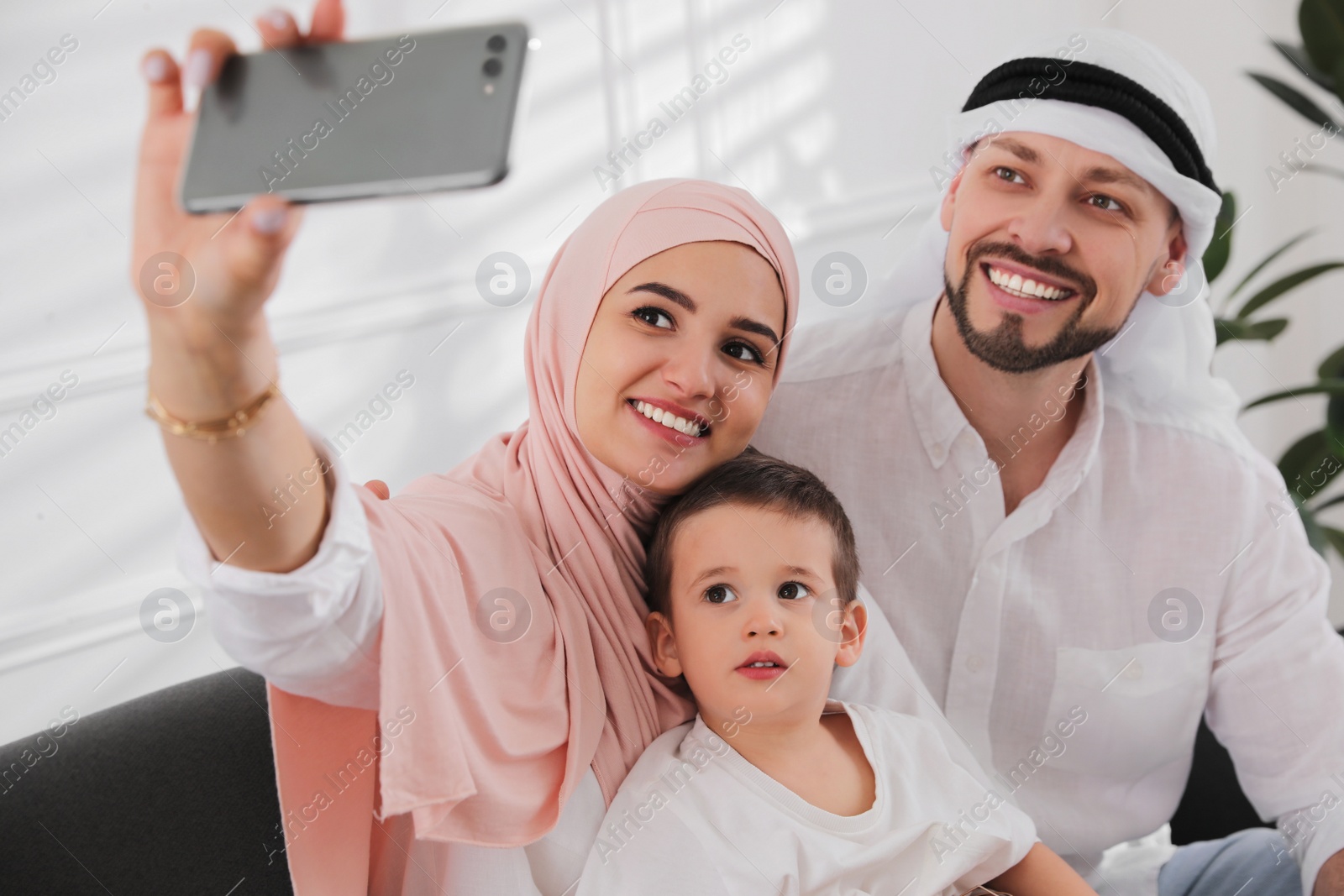 Photo of Happy Muslim family taking selfie on sofa at home