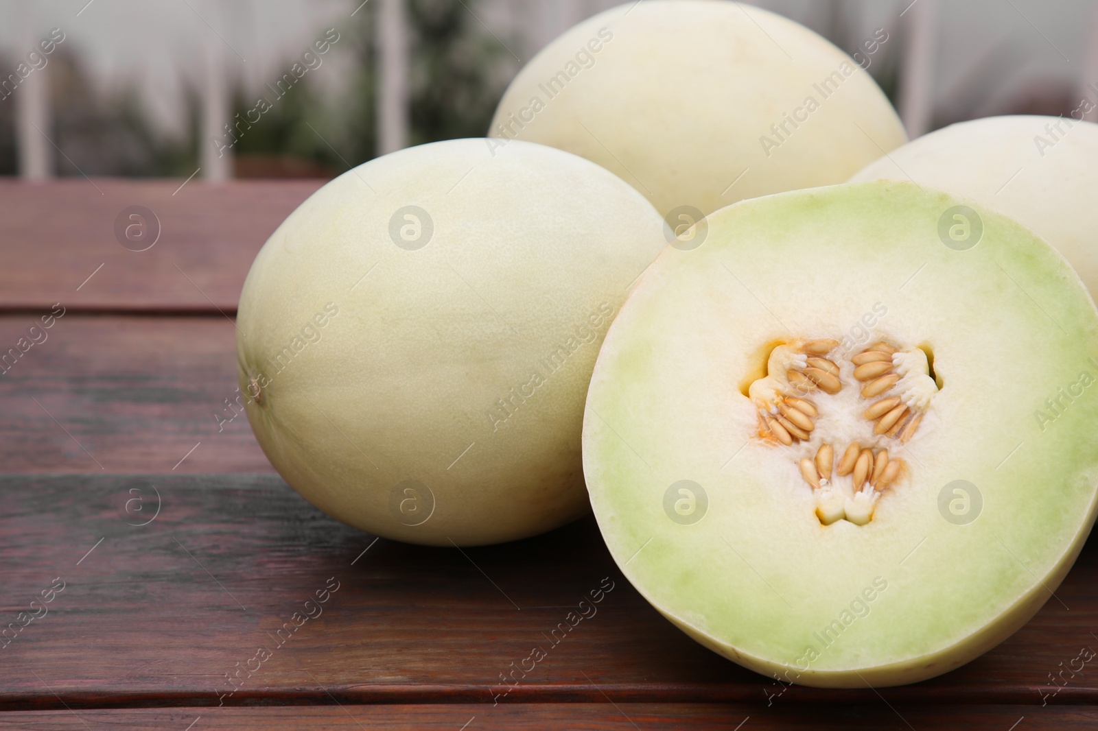 Photo of Whole and cut fresh ripe melons on wooden table outdoors