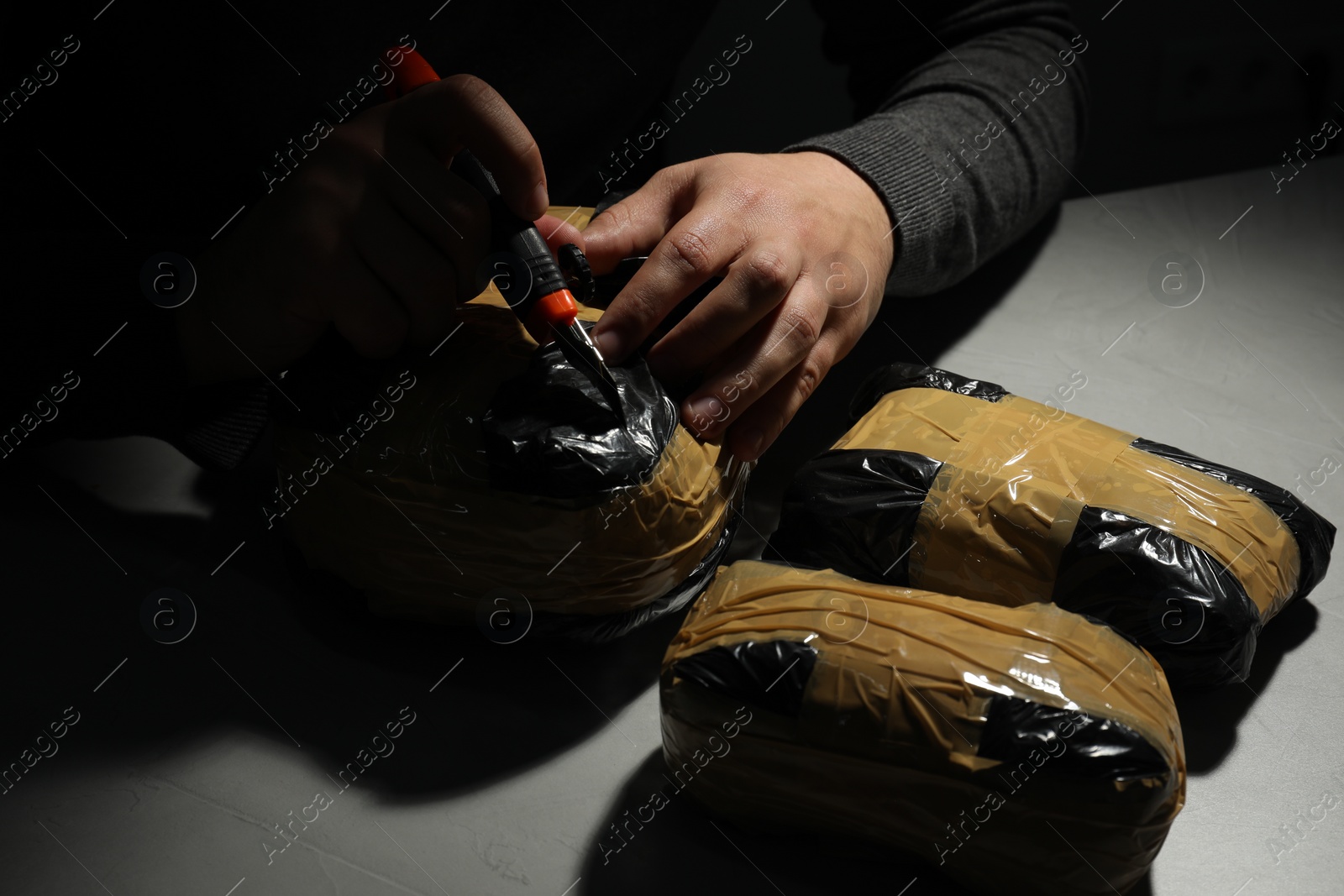 Photo of Smuggling and drug trafficking. Man opening package of narcotics with box cutter in darkness, closeup