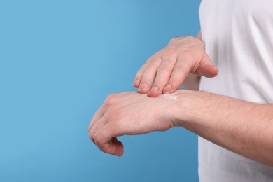 Man applying ointment onto his hand on light blue background, closeup. Space for text