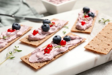 Tasty cracker sandwiches with cream cheese, blueberries, red currants and thyme on white board, closeup
