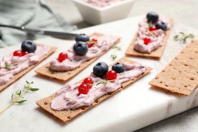 Photo of Tasty cracker sandwiches with cream cheese, blueberries, red currants and thyme on white board, closeup