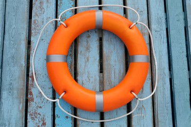 Orange life buoy on light blue wooden background, top view