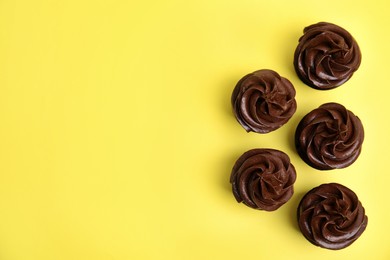 Delicious chocolate cupcakes with cream on yellow background, flat lay. Space for text