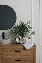 Eucalyptus branches and folded towels near stylish vessel sink on bathroom vanity. Interior design