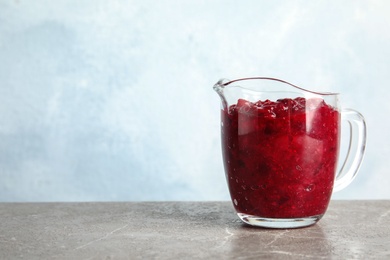 Tasty cranberry sauce in glass pitcher on table. Space for text