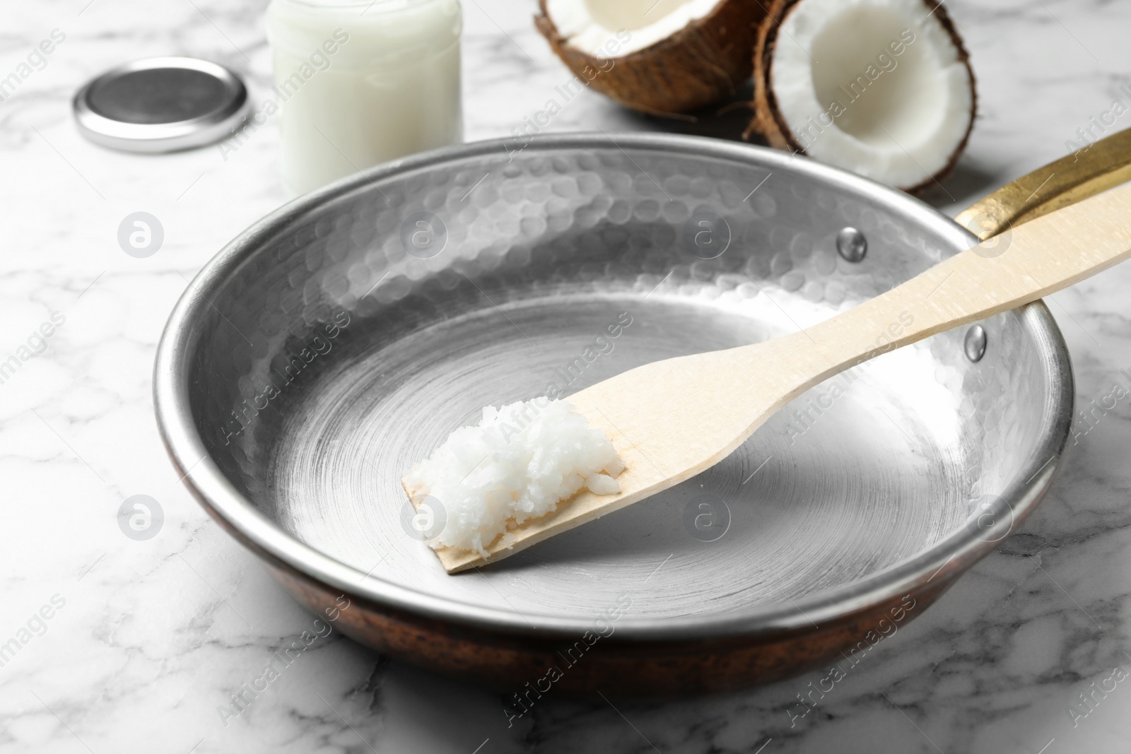 Photo of Frying pan with coconut oil and wooden spatula on white marble table, closeup. Healthy cooking