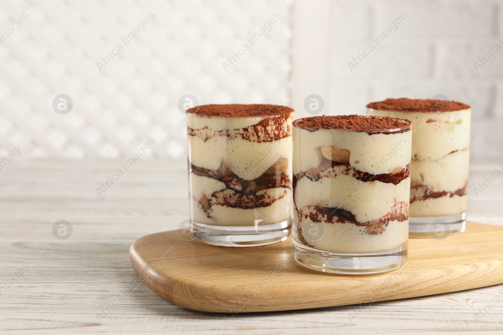 Photo of Delicious tiramisu in glasses on light wooden table. Space for text