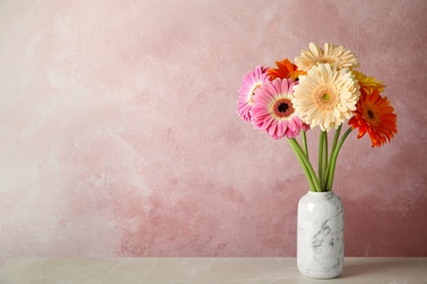 Photo of Bouquet of beautiful bright gerbera flowers in vase on marble table against color background. Space for text