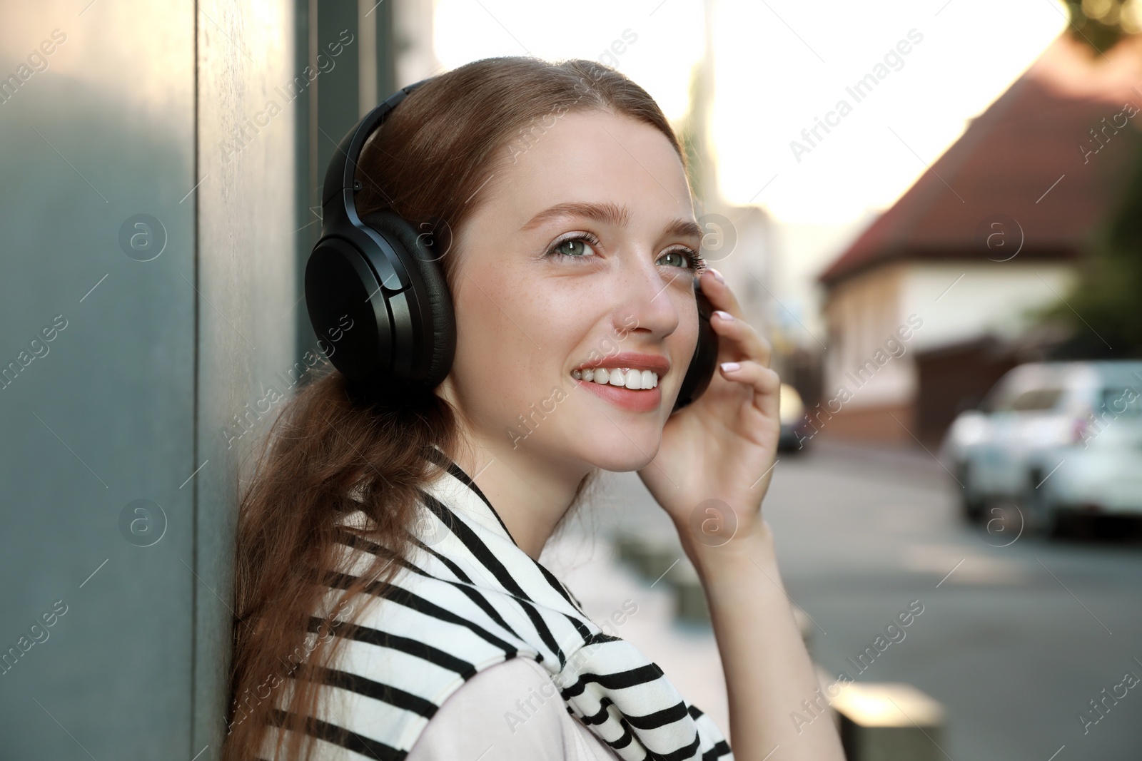 Photo of Smiling woman in headphones listening to music near building outdoors