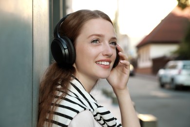 Smiling woman in headphones listening to music near building outdoors