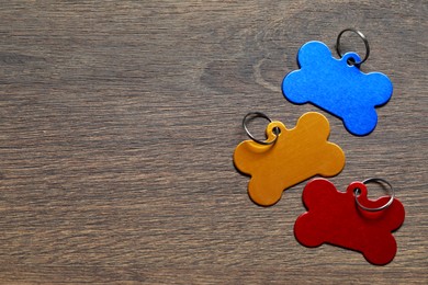 Color metal pet tags in shape of bones with ring on wooden table, flat lay. Space for text