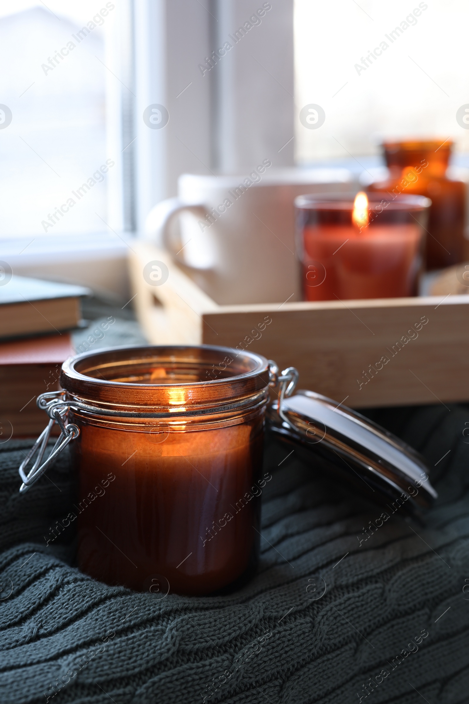 Photo of Burning candle in jar on knitted plaid near window indoors, space for text