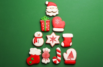 Christmas tree shape made of delicious decorated gingerbread cookies on green background, flat lay