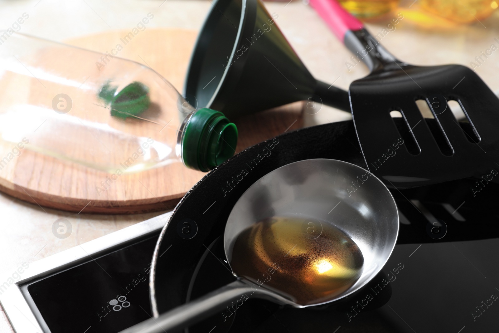 Photo of Frying pan of used cooking oil with ladle, empty bottle and funnel in kitchen, closeup