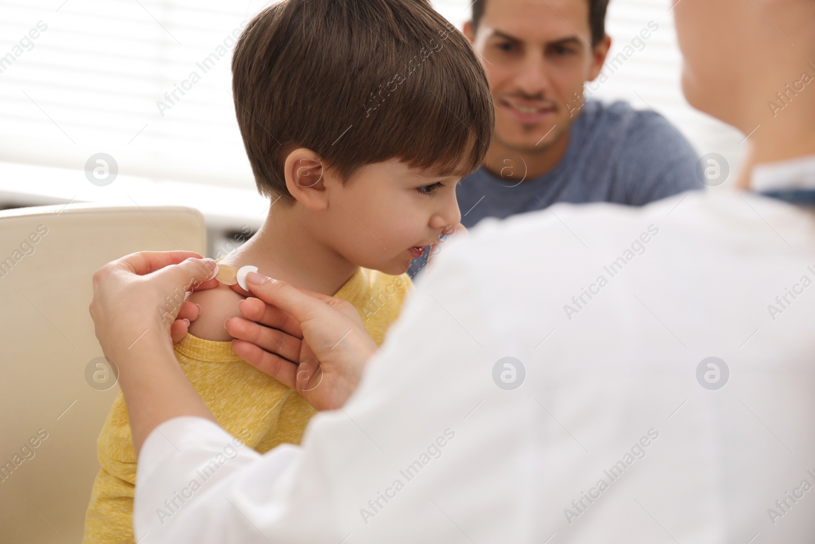 Photo of Doctor putting sticking plaster onto little boy's shoulder indoors
