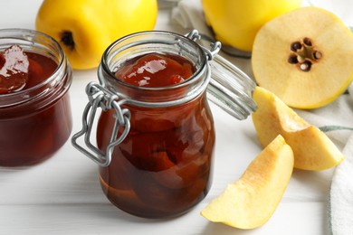 Photo of Tasty homemade quince jam in jars and fruits on white wooden table, closeup