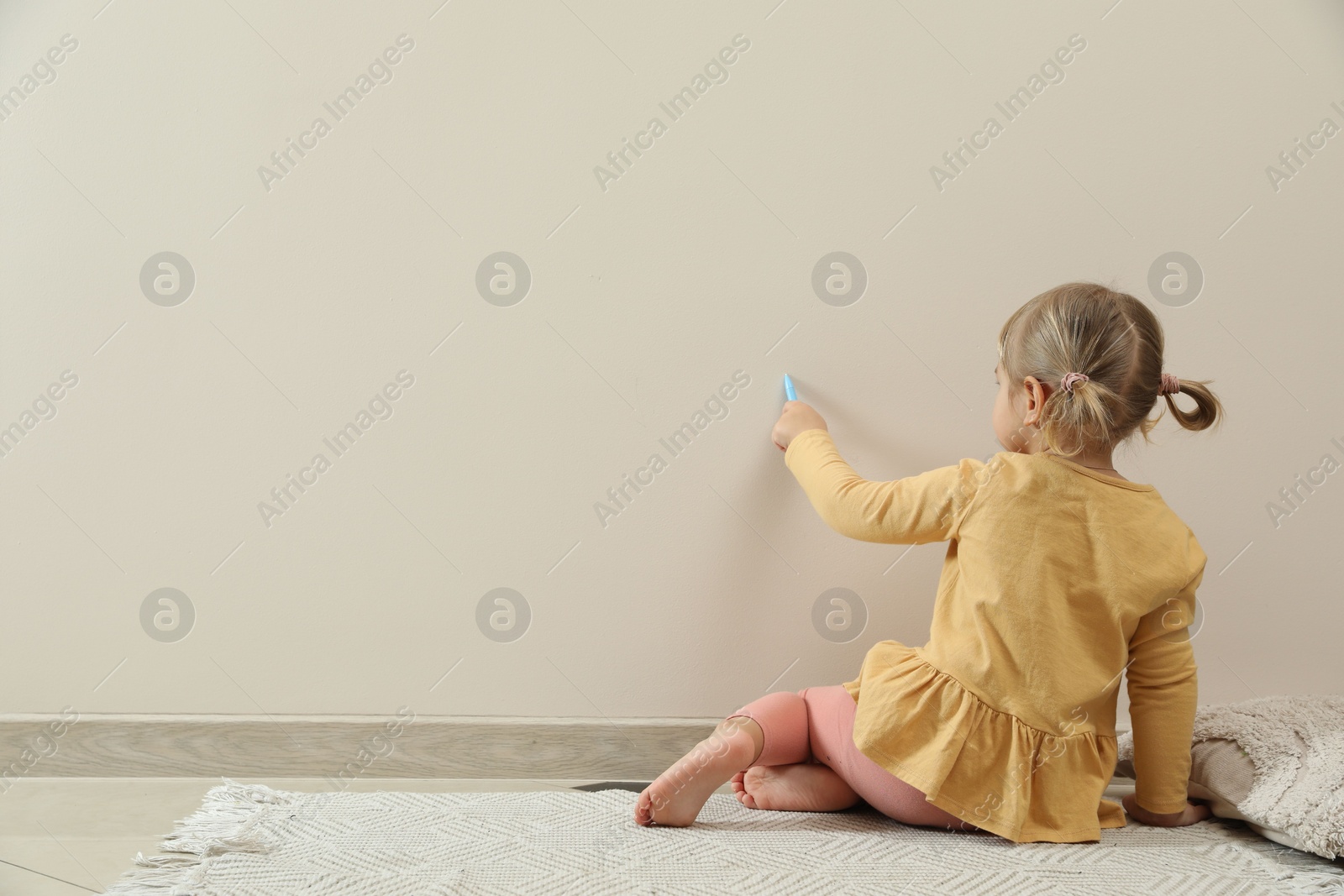 Photo of Little girl drawing on beige wall indoors, back view and space for text. Child`s art