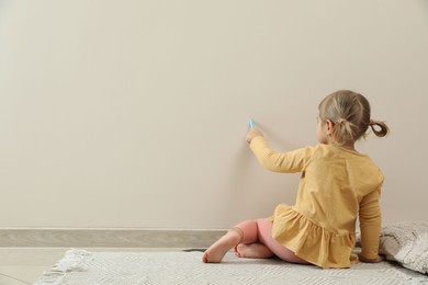 Little girl drawing on beige wall indoors, back view and space for text. Child`s art