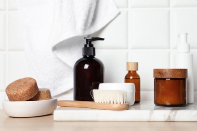 Photo of Different bath accessories and personal care products on wooden table near white tiled wall