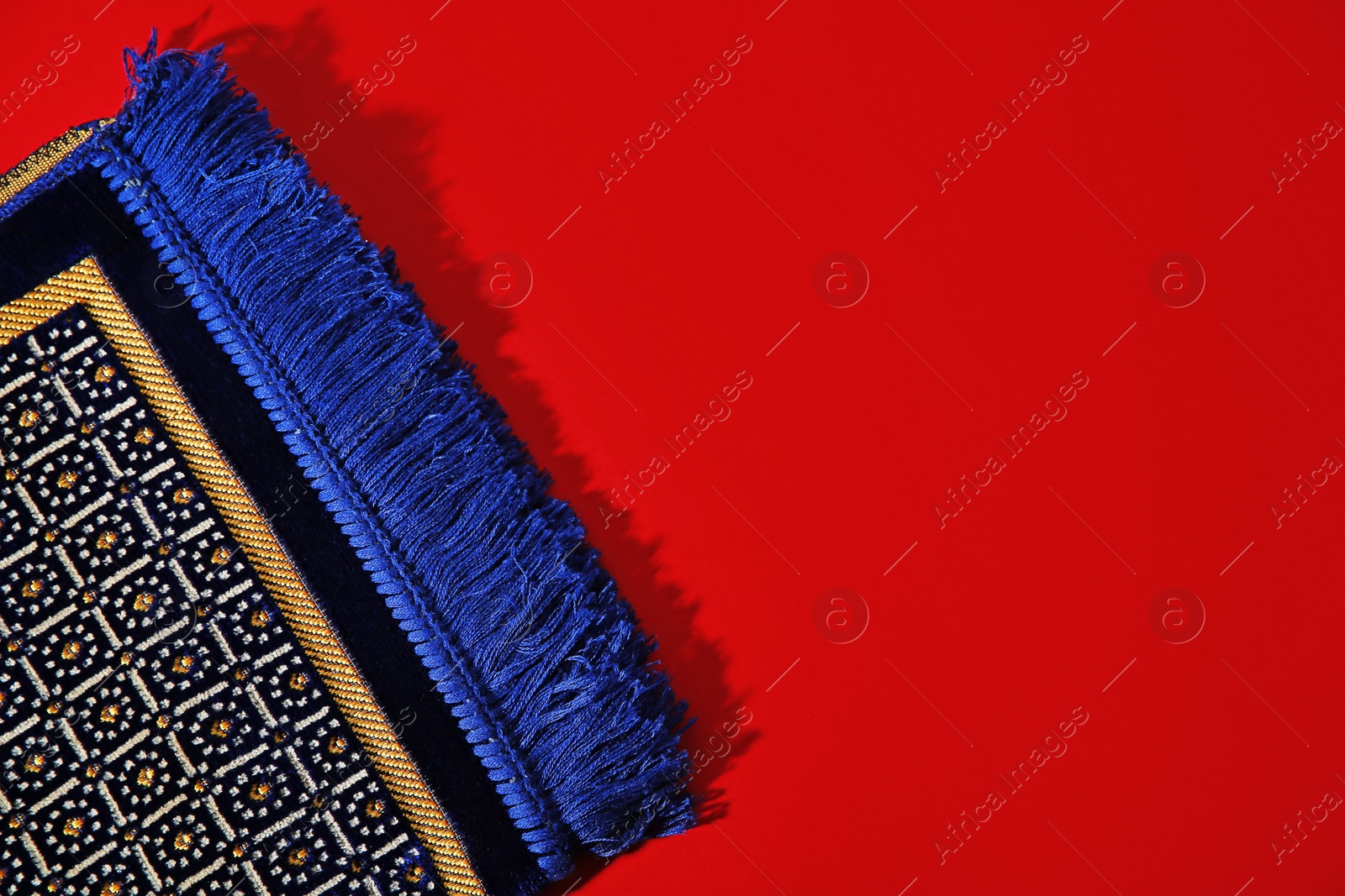 Photo of Muslim prayer rug and space for text on color background, top view