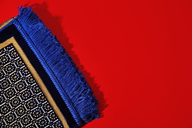 Photo of Muslim prayer rug and space for text on color background, top view