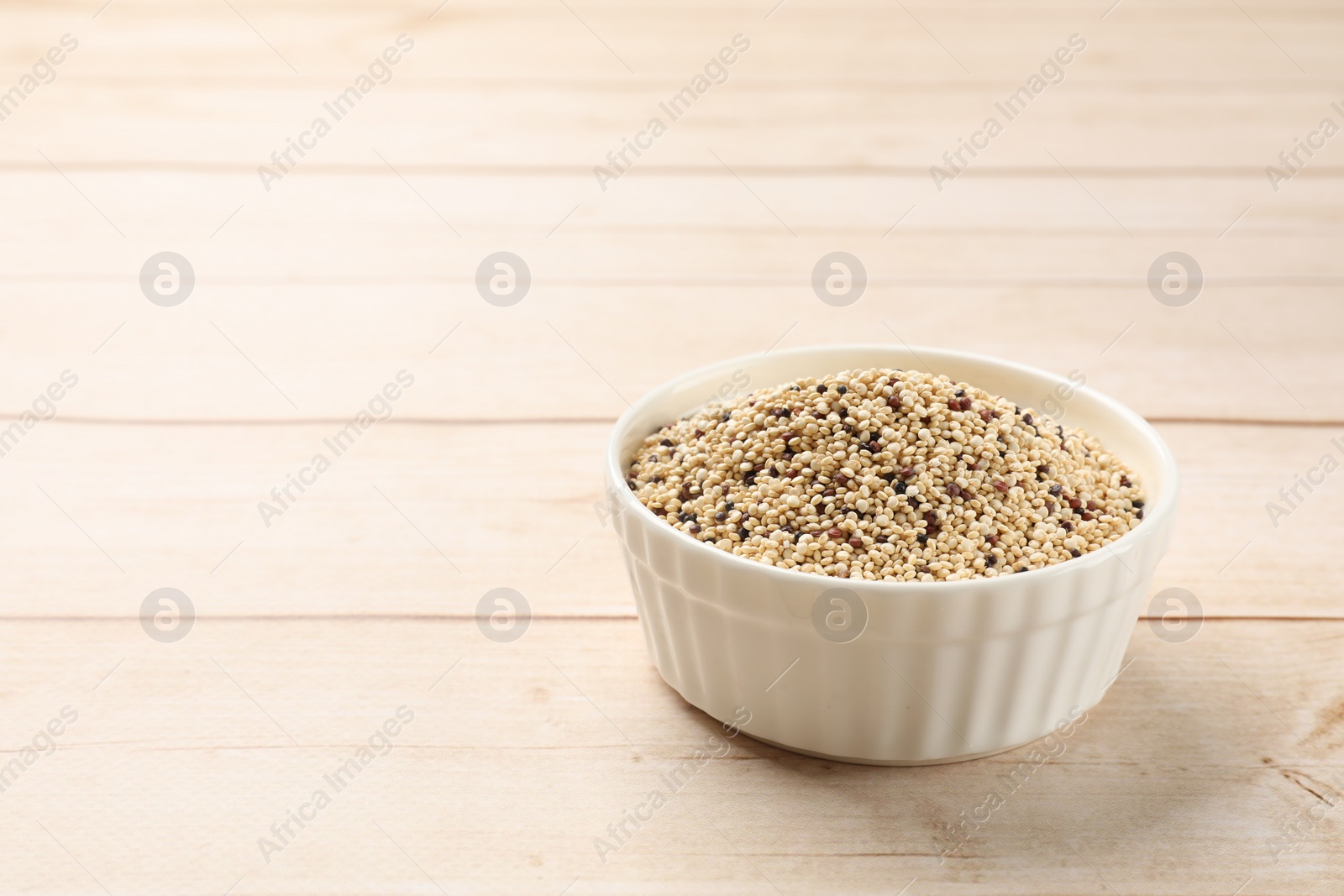 Photo of Raw quinoa seeds in bowl on wooden table. Space for text