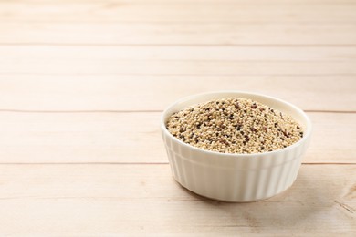 Photo of Raw quinoa seeds in bowl on wooden table. Space for text
