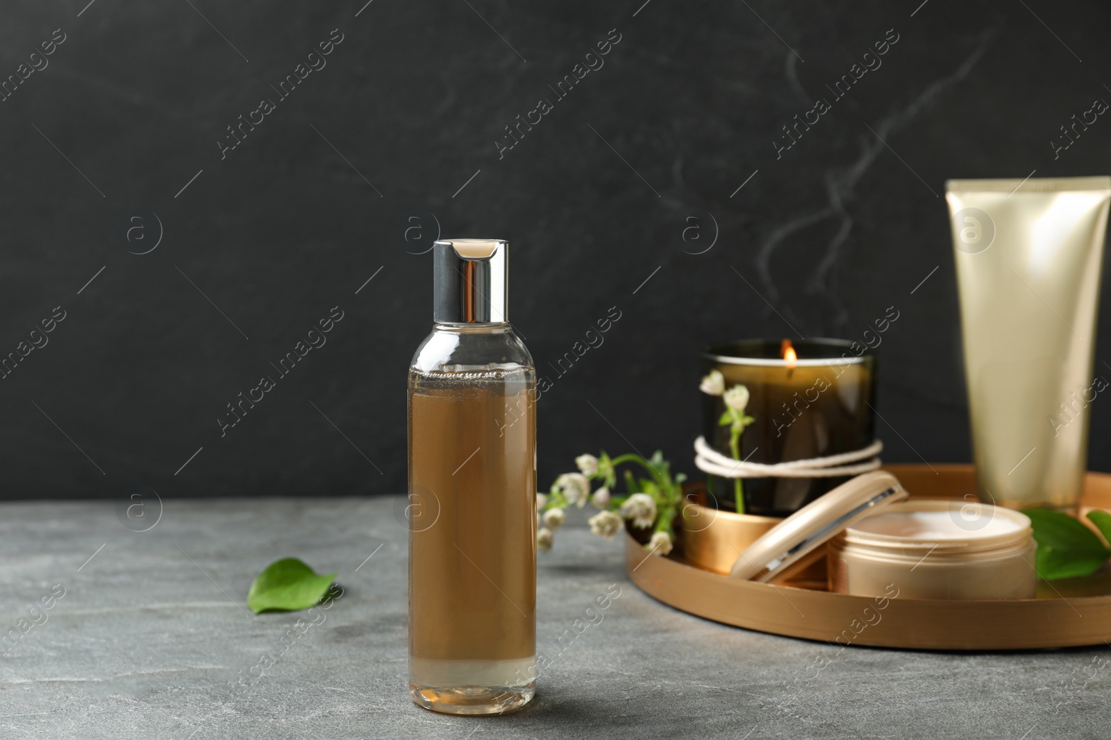 Photo of Cosmetic products and burning candle on grey stone table