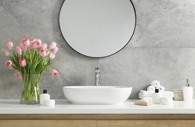 Photo of Vase with beautiful pink tulips and toiletries near sink in bathroom