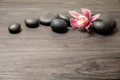 Photo of Spa stones with orchid flower on wooden background. Space for text