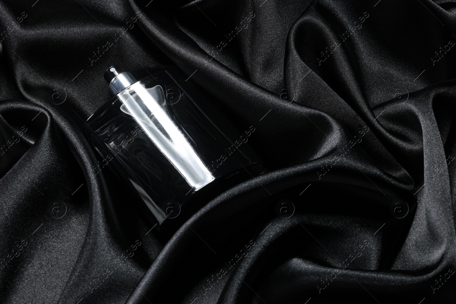 Photo of Luxury men's perfume in bottle on black satin fabric, above view. Space for text